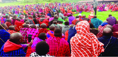 People in various shades of vibrant red, pink, blue and purple sitting on the grass around one speaker